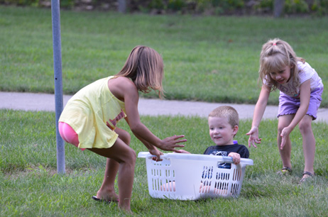 Two Girls Pulling & Pushing a Small Boy in Laundry Basket